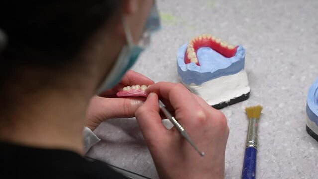 Making of dental prosthetic and carving out dents in artificial wax gums with scalpel at the workstation by healthcare worker