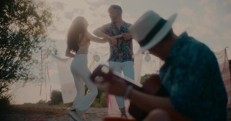 Young man playing guitar for couple dancing at beach - Powered by Adobe