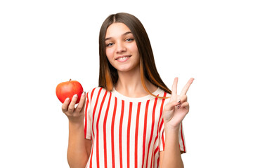 Teenager girl with an apple over isolated chroma key background smiling and showing victory sign