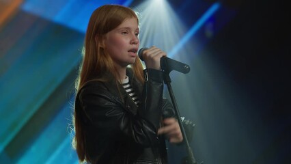Young teenager girl singer performing on stage, contestant singing during recording of television style broadcast talent show