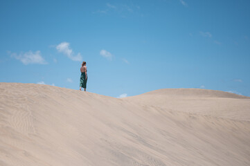 A blonde young girl in a green dress in the distance walking along the crest of the dune