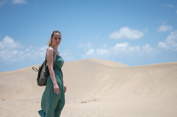 A blonde young girl in a green dress and backpack on the beach dunes