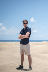 Blond young boy with crossed arms sunglasses on the beach dunes