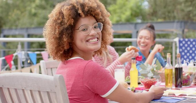 Portrait of biracial woman sitting at dinner table with diverse friends in garden, slow motion