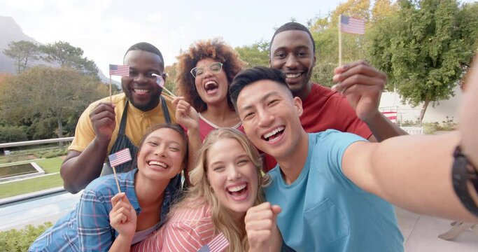 Happy diverse group of friends holding flags of usa and taking selfie in garden, slow motion