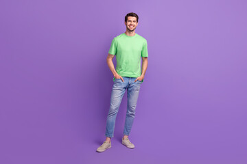 Fototapeta premium Full length photo of young guy wear green t-shirt jeans denim sneakers stylish outfit advertisement isolated on purple color background