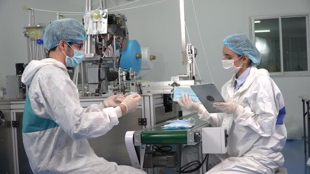 worker man and woman in ppe suit using tablet inspecting quality control surgical face mask in production line at industry  factory.