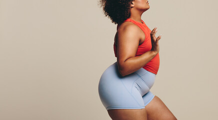 Woman with a fit, plus size body stands in a studio confidently, wearing fitness clothing
