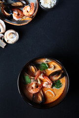 Tom Yam soup with coconut milk with shrimp, squid, mussels and mushrooms. Vertical photo on a dark backgroundFlat lay. Top view. Copy space..