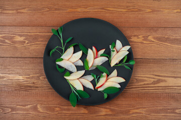 Obraz na płótnie Canvas Beautifully sliced fruits, apples. Laid out in the form of a flower for a festive table. Salad of whole and chopped vegetables. on a round black plate. close-up. on a wooden background 