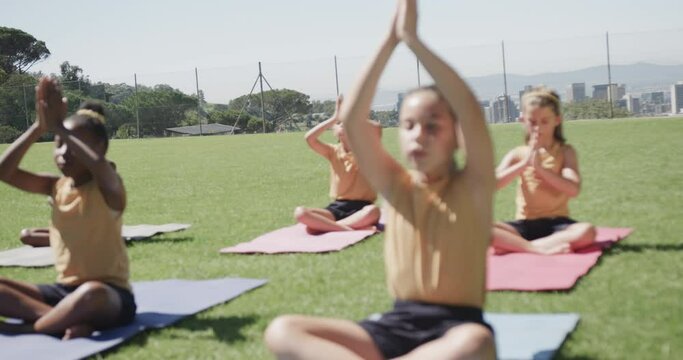 Focused diverse elementary school schoolgirls practicing yoga at stadium in slow motion