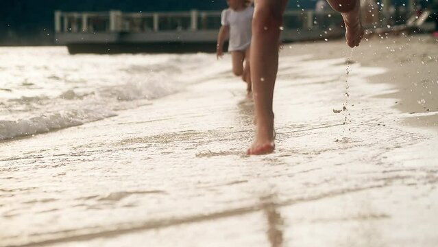 Two little girls run barefoot on the beach, slow motion tele lens shot