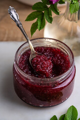 Glass jar with homemade edible rose jam on marble-wooden board..