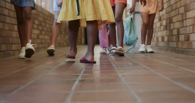 Diverse schoolgirls with school bags walking at elementary school corridor in slow motion