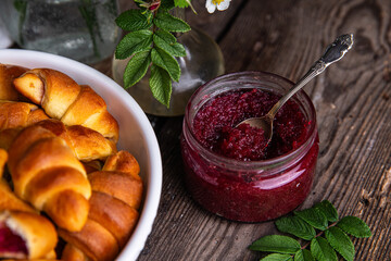 Glass jar with homemade edible rose jam and crescents with rose jam on old wooden table.