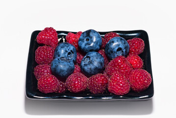 Sweet fresh organic raspberries and blueberries in a black plate on a white background