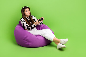 Full length photo of funky unsure girl dressed cowskin top bean bag playing playstation empty space isolated green color background © deagreez
