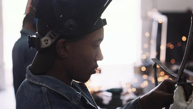 Young black male profile working on steel structure in workshop with sparks bokeh slow motion