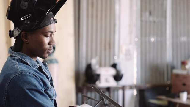 Slow motion of young black male in welding gear lifting steel structure