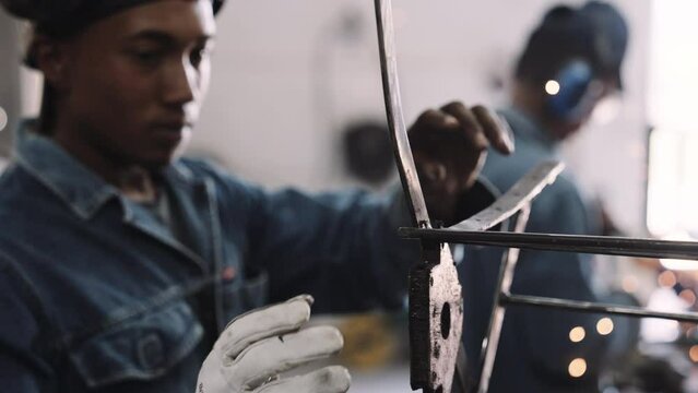 Young black male working on steel structure with welding gear and gloves in workshop slow motion