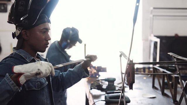 Young black males in denim jackets working with steel in open workshop medium close up slow motion