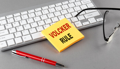 VOLCKER RULE text on a sticky with keyboard, pen glasses on grey background