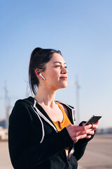 vertical portrait of a beautiful female runner playing music on mobile phone using earphones, concept of technology and sportive lifestyle