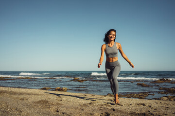 Fototapeta na wymiar a beautiful athletic brunette girl in a gray tracksuit walks barefoot on the sand against the backdrop of the sea
