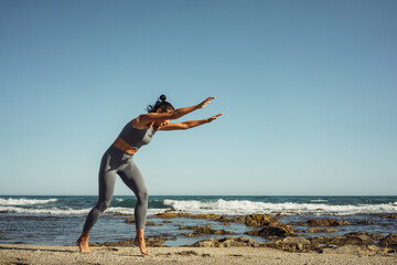 a beautiful brunette girl in gray leggings is engaged in fitness on the sand against the background of the sea