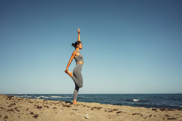 a beautiful brunette girl in gray leggings is engaged in fitness on the sand against the background of the sea