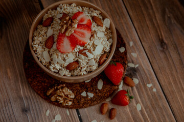Oatmeal porridge with strawberries and nuts on dark wooden background