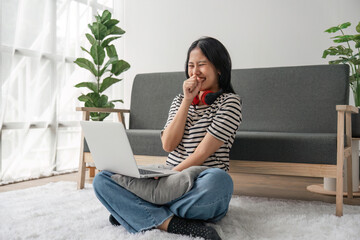 Asian woman happily using laptop to watch comedy series at home