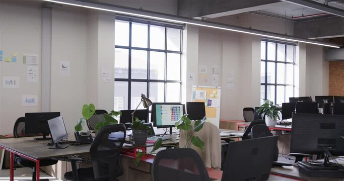 Office workspace with large windows, chairs and desks with computers, lamps and plants, slow motion