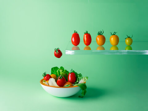 Row of assorted multi coloured tomatoes jumping off a diving board into a bowl of salad