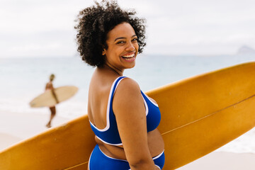 Female surfer smiling on the beach, holding surfboard ready for adventure