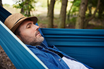 Man taking a nap sleeping in hammock in forest during summer vacation