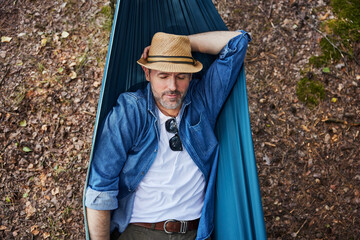 Overhead portrait of handsome adult man sleeping in hammock in forest taking nap during hiking trip