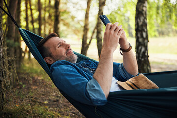 Adult man in hammock using smart phone browsing internet during summer vacation