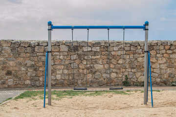 swing with two seats in an outdoor plaza with a stone wall behind it