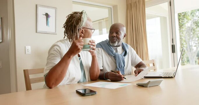African american senior couple doing paperwork using laptop at home, slow motion