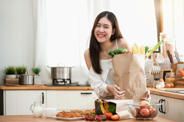 Happy young Asian woman in the kitchen and grocery shopping bag with vegetables