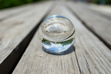 Glass lens ball on weathered wood boards reflecting trees and blue sky