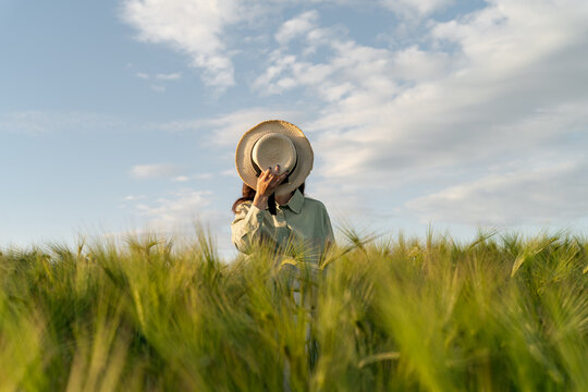 Woman standing in a field covering her face with a straw hat, Belarus