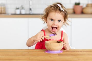 Funny toddler girl eating chocolate mousse with spoon