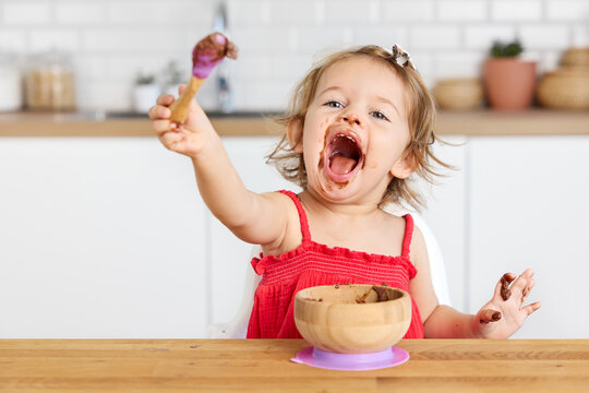 Naklejki Funny toddler girl making funny face while eating chocolate mousse