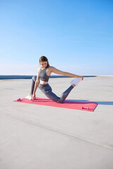 Young beautiful woman in comfortable grey sportswear training, doing stretching exercises on warm morning outdoors