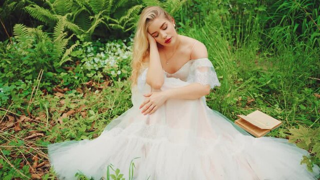 Art fairy tale sleeping beauty face girl princess blue eyes closed. Fantasy woman lies on green grass summer nature bed flowers. white medieval vintage dress. Blonde hair sexy lady read novel book. 4k
