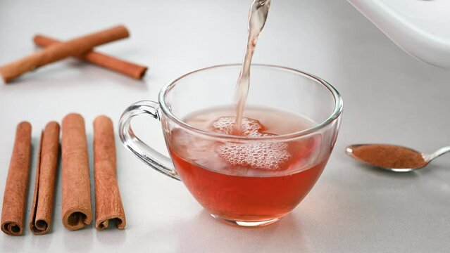 Serving cinnamon water in a glass cup with cinnamons in the background.