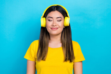 Photo of cheerful pleasant girl with straight hairdo dressed yellow t-shirt enjoy favorite songs isolated on blue color background