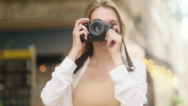 Portrait of pretty blond woman photographer looking at camera hold digital camera and take photo at urban city street Charming young tourist female taking pictures outdoors